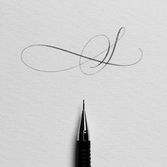 an ink pen is laying on top of a piece of paper that has the letter l written in cursive writing