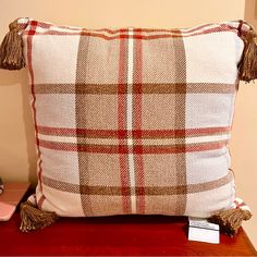 a plaid pillow with tassels sits on a table next to a pink vase