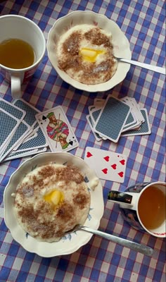 two bowls of food on a table with playing cards and cups of tea next to them