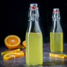 two glass bottles filled with liquid next to sliced oranges