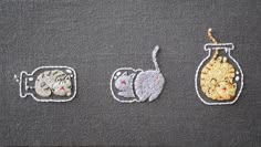 three embroidered images of cats in glass jars on a gray surface with white stitching