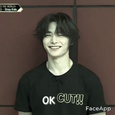 a young man wearing a black shirt with the words ok cut on it in front of a red wall