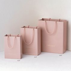 three pink shopping bags sitting next to each other on a white surface, with the same bag in front of them