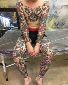 a man with tattoos on his body sitting on a stool in front of a bed