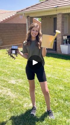 a woman standing in the grass holding up a piece of paper and some kind of object