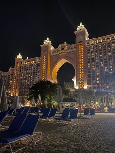 the hotel is lit up at night with beach chairs and umbrellas on the sand