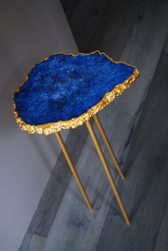 a blue and gold table with two legs on the floor in front of a white wall