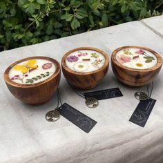 three wooden bowls filled with food sitting on top of a cement table next to tags