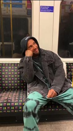 a man sitting on a subway train with his head in his hands and looking at the camera