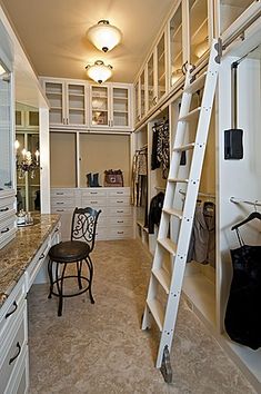 a ladder is in the middle of a walk - in closet with white cabinets and drawers