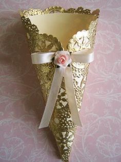 a gold vase with a pink flower and ribbon tied around the top on a table