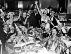 a group of people sitting at a table with hats on and holding up their hands