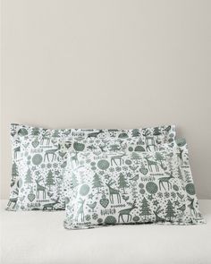 two pillows sitting on top of a bed covered in green and white christmas themed fabric