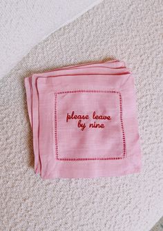 a pink cloth with embroidered words on it sitting on the floor next to a white rug