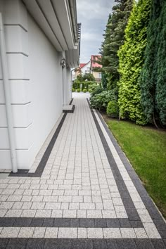 a brick walkway between two white buildings with trees in the back ground and grass on either side