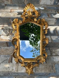 an ornate gold mirror on the side of a brick wall with a tree in the reflection