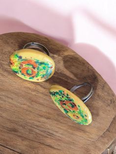 two rings are sitting on top of a wooden stand with flowers painted on them and one is yellow, the other is green