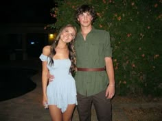 a man and woman standing next to each other in front of a tree at night