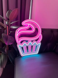 there is a neon sign that says cupcake on the table next to a potted plant