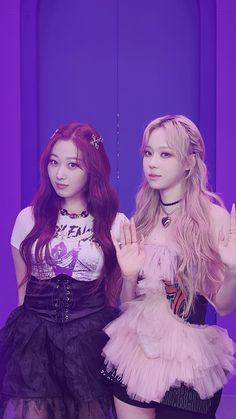 two young women standing next to each other in front of a purple wall and holding their hands up