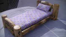 a small wooden bed with purple and white polka dot sheets on it's sides