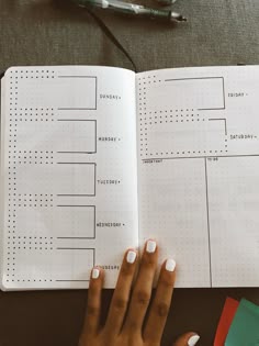 a person's hand on top of a notebook with a planner in the background