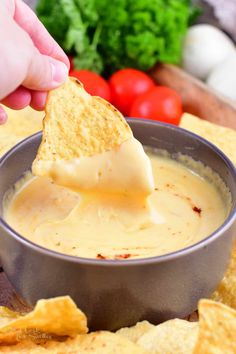 a person dipping cheese into a bowl of quesadilla sauce with tortilla chips