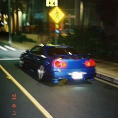 a blue car is driving down the street at night