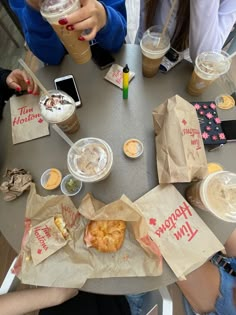 several people sitting at a table with food and drinks in their hands, one holding a cell phone