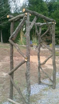 a wooden structure made out of sticks and logs in the middle of a field with trees behind it