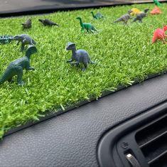 small toy dinosaurs in the grass on top of a car dashboard dash mat, with green grass