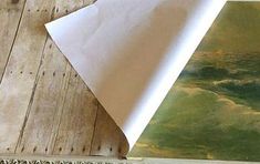 a piece of white paper sitting on top of a wooden floor next to a painting