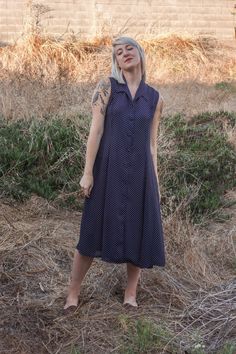 "this gorgeous vintage dress appears to be 50's inspired, with 70's boho flair. a dark navy blue with  white polka dots, collar, and white buttons down the entire front, the dress is also a bit sheer (see photos). will look nice with a slip underneath, and even with a belt to cinch in the waist (not pictured). appears to be in wonderful conditions despite its age, and would look gorgeous with some brown espadrille sandals or vintage heels - or make it casual, and pair it with some vintage lace-u Fitted Vintage Dress For Dress Down Summer, Fitted Vintage Dress For Summer Dress-down, Fitted Vintage Dress For Dress Down Summer Events, 1950s Style Fitted Dress With Buttons, 1950s Style Polka Dot Dresses For Spring, Spring Polka Dot Vintage Dress, Navy Fitted Vintage Dress, Summer Collared Fitted Midi Dress, Classic Summer Dresses With Button Closure