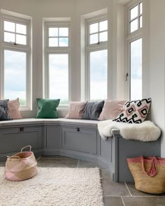 a corner window seat with pillows on it in front of two windows and a rug