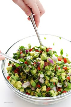 a person is cutting into a salad in a glass bowl with silver spoons on the side