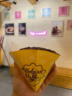 a person holding up a paper cone with chocolate on it in front of a wall