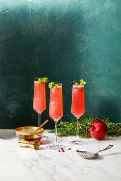 three wine glasses filled with fruit and garnish on a marble countertop next to silverware