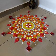 a colorful rangdi design on the floor in front of a vase and candle holder