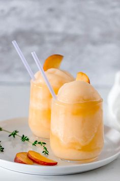 two glasses filled with orange juice and garnished with sliced peaches on a white plate