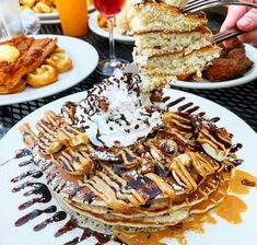 a stack of pancakes topped with whipped cream and chocolate syrup being lifted from the top