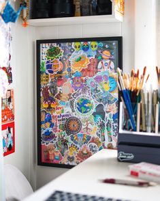 an art work is displayed on the wall above a desk with pens and pencils