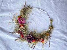 a wreath made out of dried grass and flowers on a white sheeted surface with the letter o in the middle