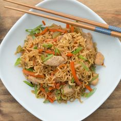 a white plate topped with noodles and meat next to chopsticks on a wooden table