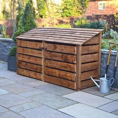 a wooden storage shed sitting on top of a stone floor next to a garden area