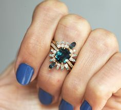 a woman's hand holding a ring with an emerald and white diamond on it