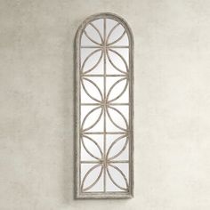 a mirror hanging on the wall in front of a white wall with an arched window