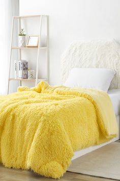 a bright yellow fluffy blanket on a bed in a room with white walls and wooden floors