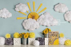 a table topped with vases filled with yellow and white flowers next to paper clouds