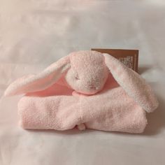 a pink stuffed animal laying on top of a white bed sheet with a tag hanging from it's ear