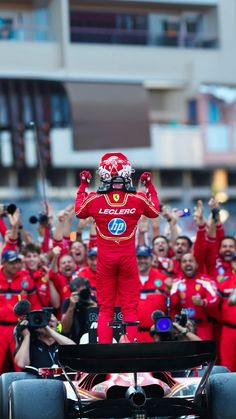 a man standing on top of a race car in front of a group of people